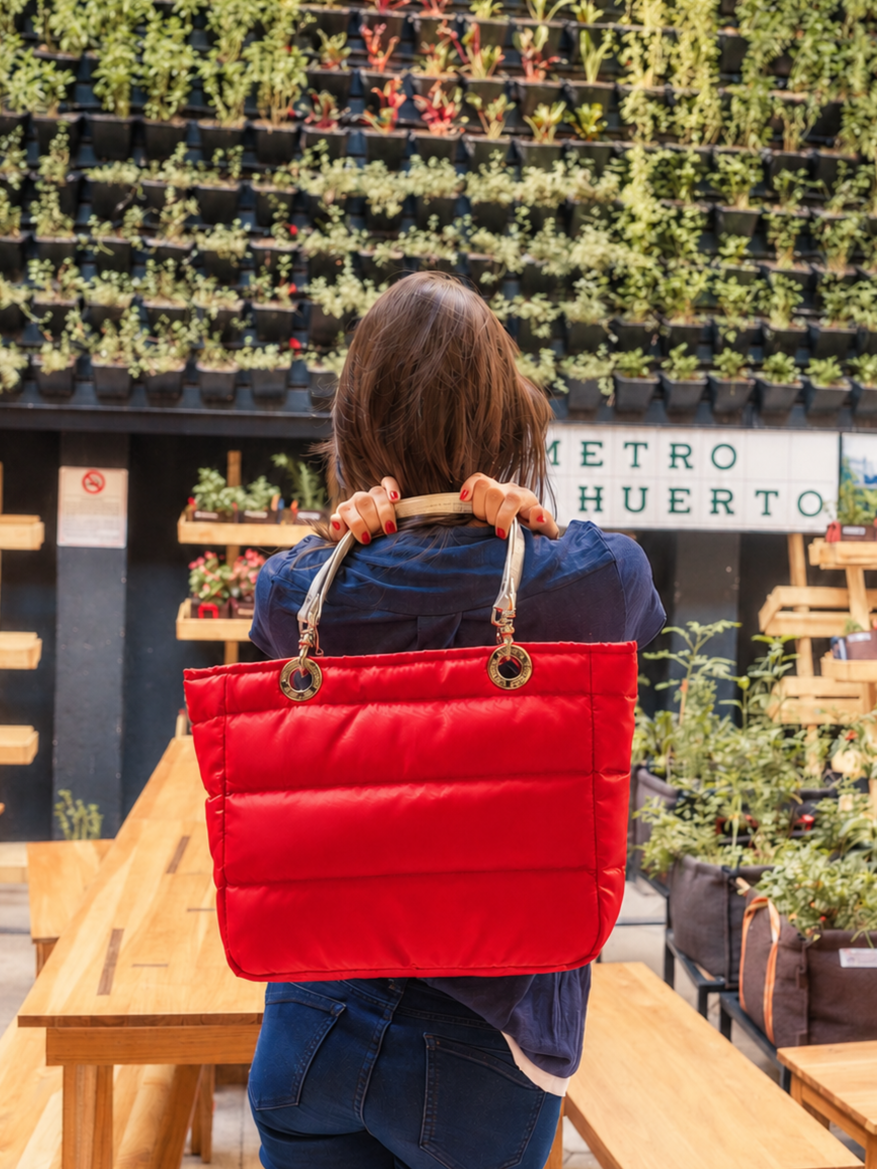 Mujer con una bolsa B&aacute;sica Sundar roja frente a un jard&iacute;n vertical
